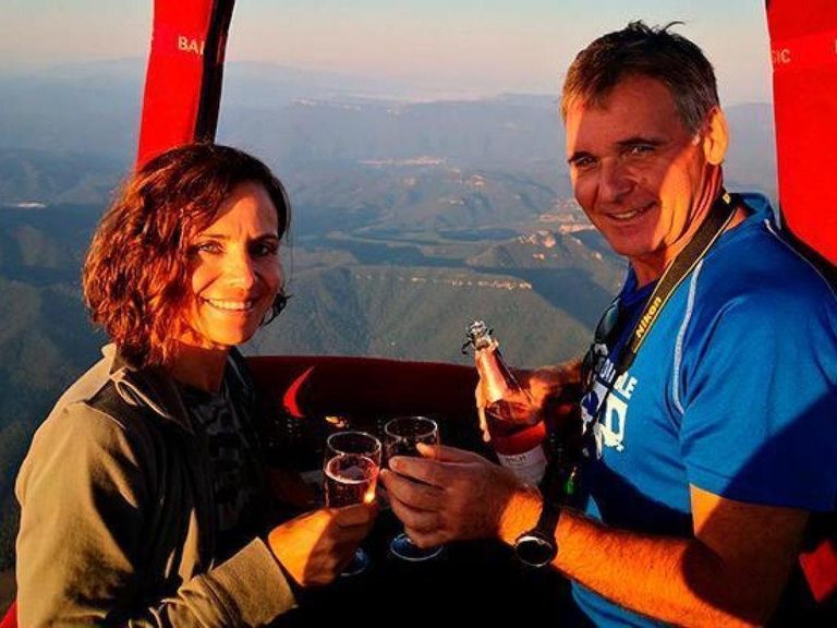 A couple raising glasses together in a balloon basket with hills in the distance