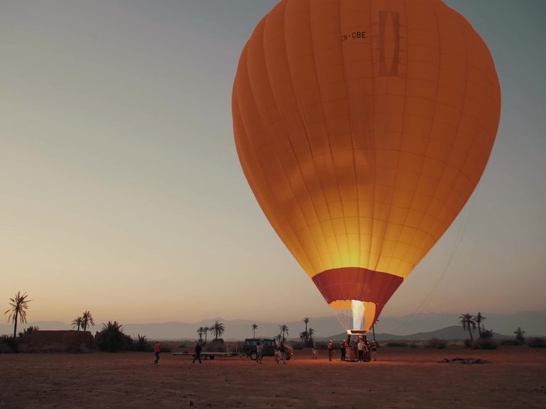 An inflated hot air balloon standing upright on the launch field before sunrise