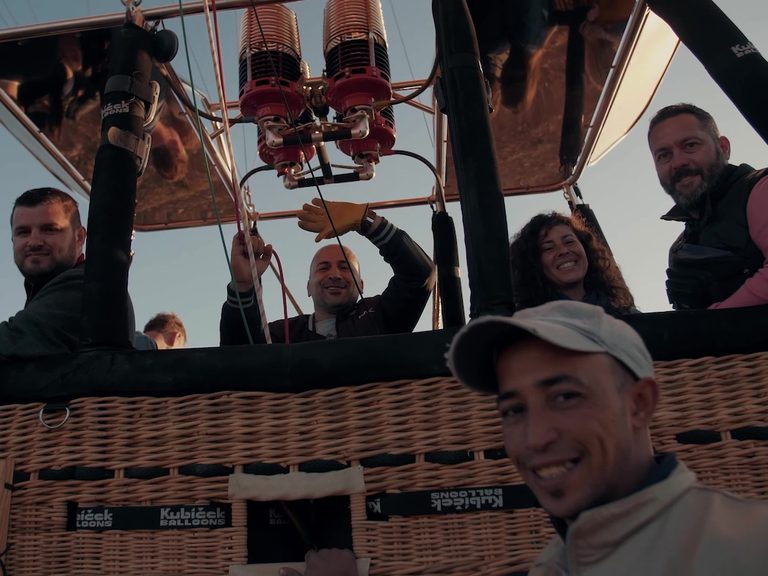 Passengers standing together inside a wicker balloon basket during a flight
